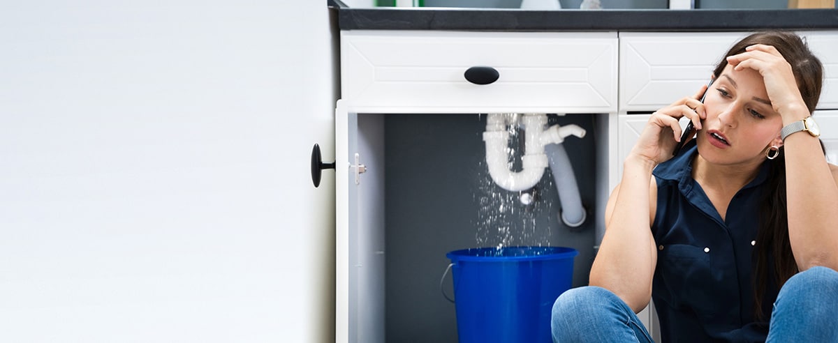 Woman talking on a cell phone in front of a leaking sink drain