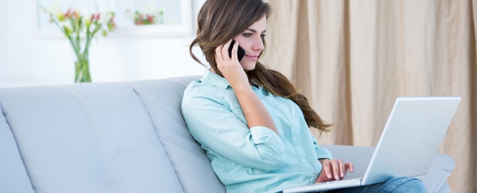 Woman sitting on a couch looking at her laptop making a phone call